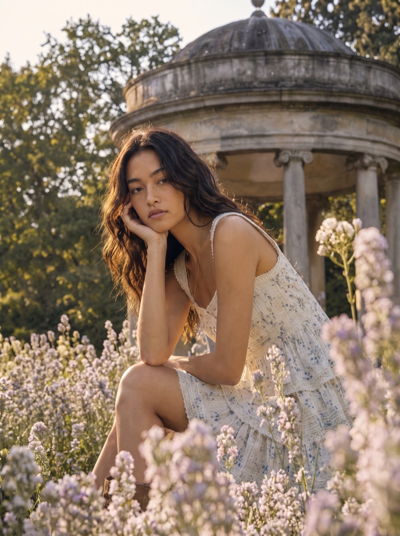 Previs frame: the model in a tiered white dress, seated among the flowerbeds below the rotunda